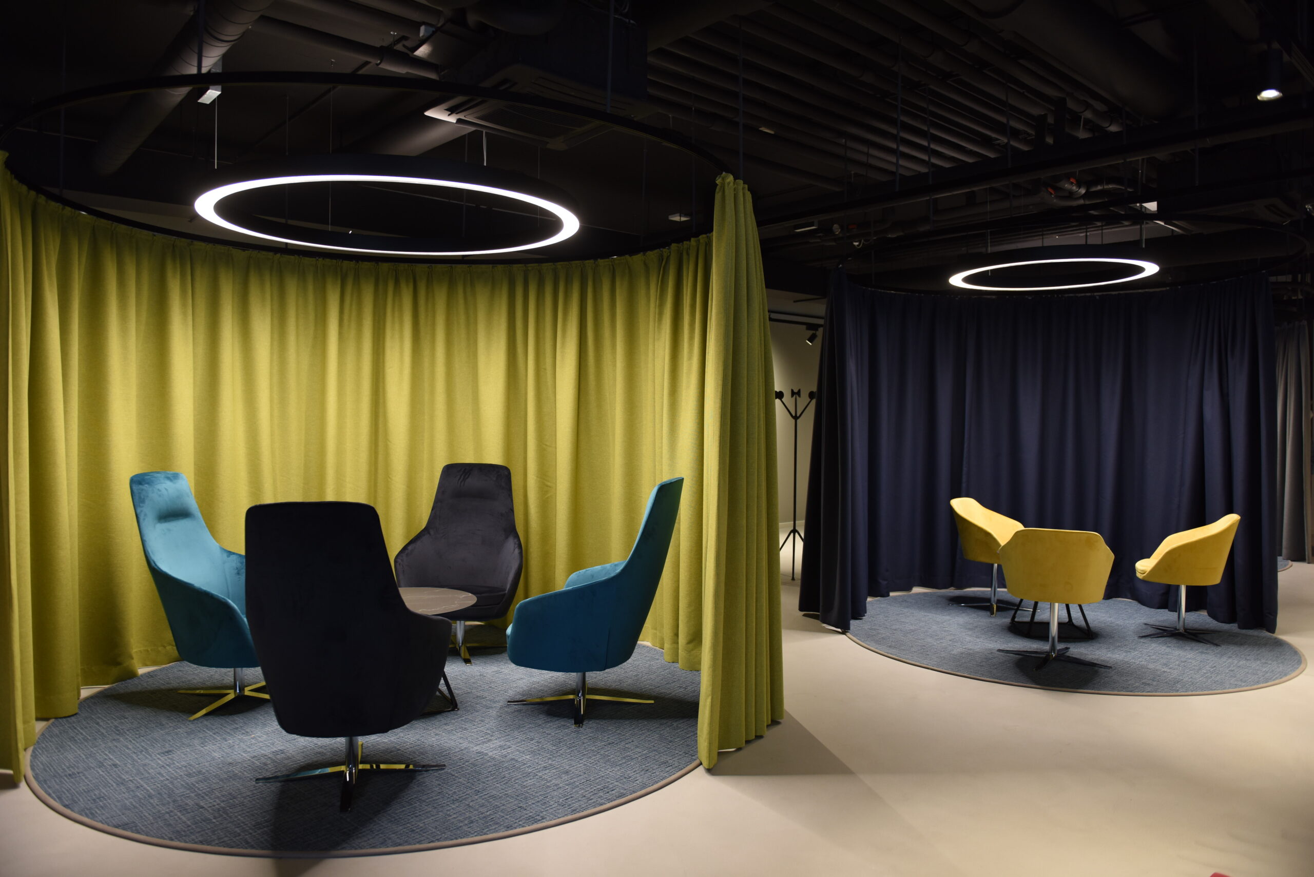 Due isole di poltrone colorate con tende circolari e anelli luminosi LED in ambiente scuro industriale.
