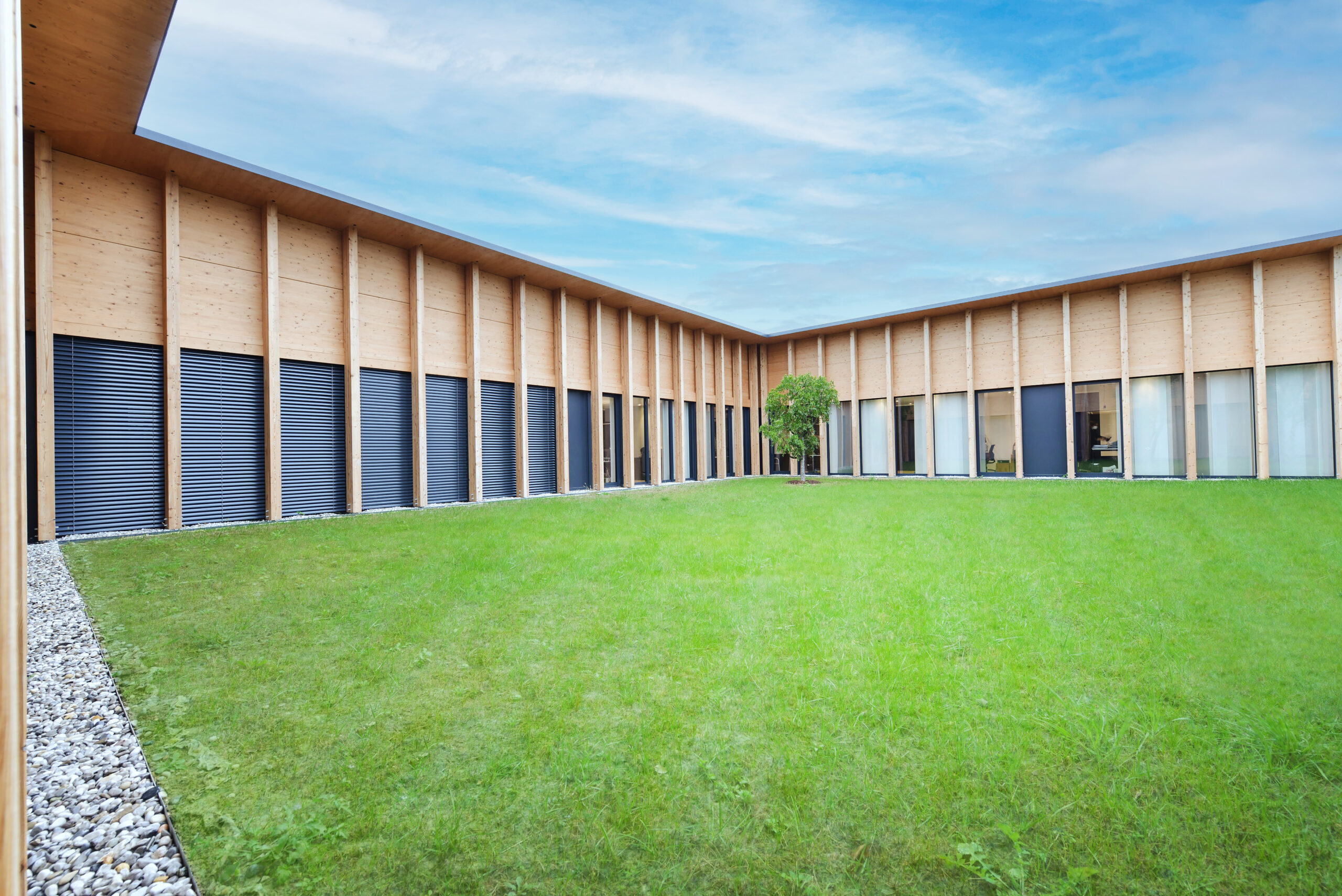 Patio centrale a prato con facciata in larice e serramenti verticali: corpo “ad abbraccio” che porta luce naturale agli uffici interni.