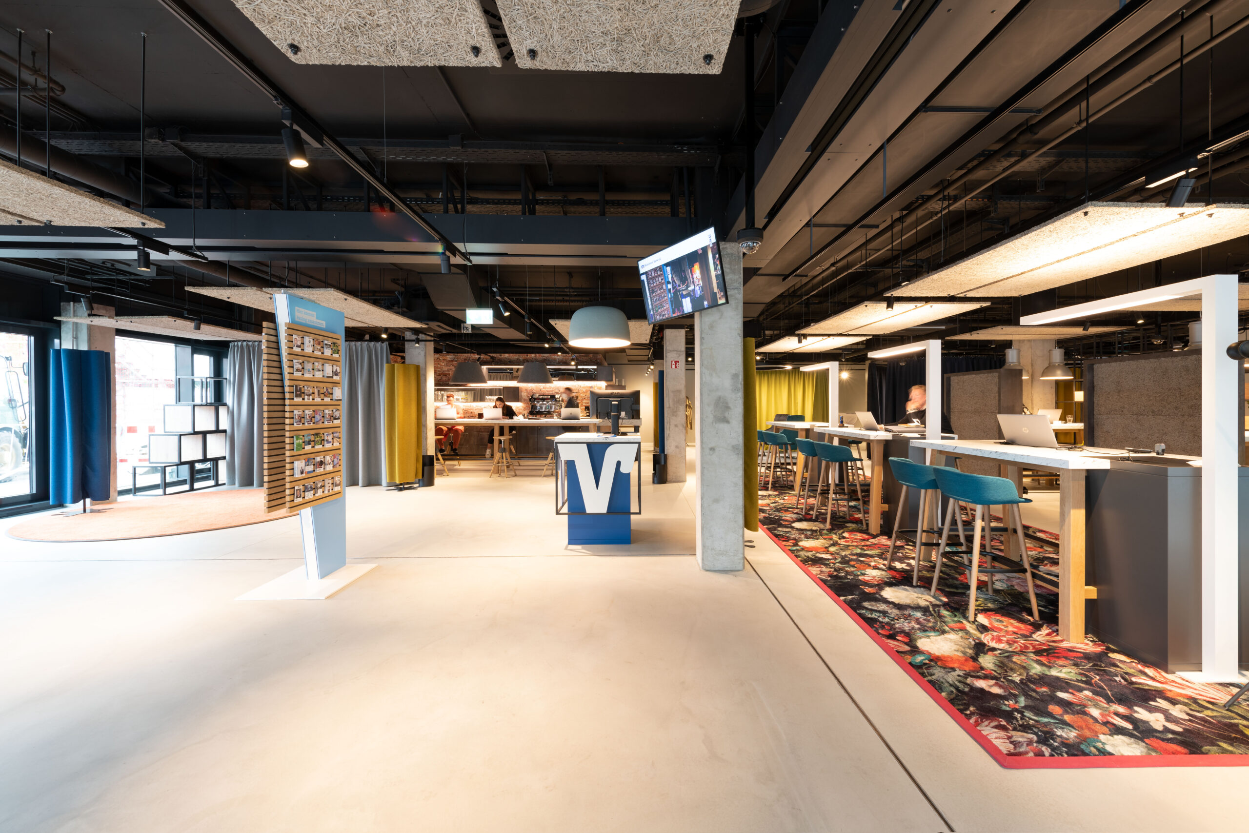 Ingresso con totem informativo girevole, bancone bar e percorsi definiti da moquette floreale e sgabelli turchesi.