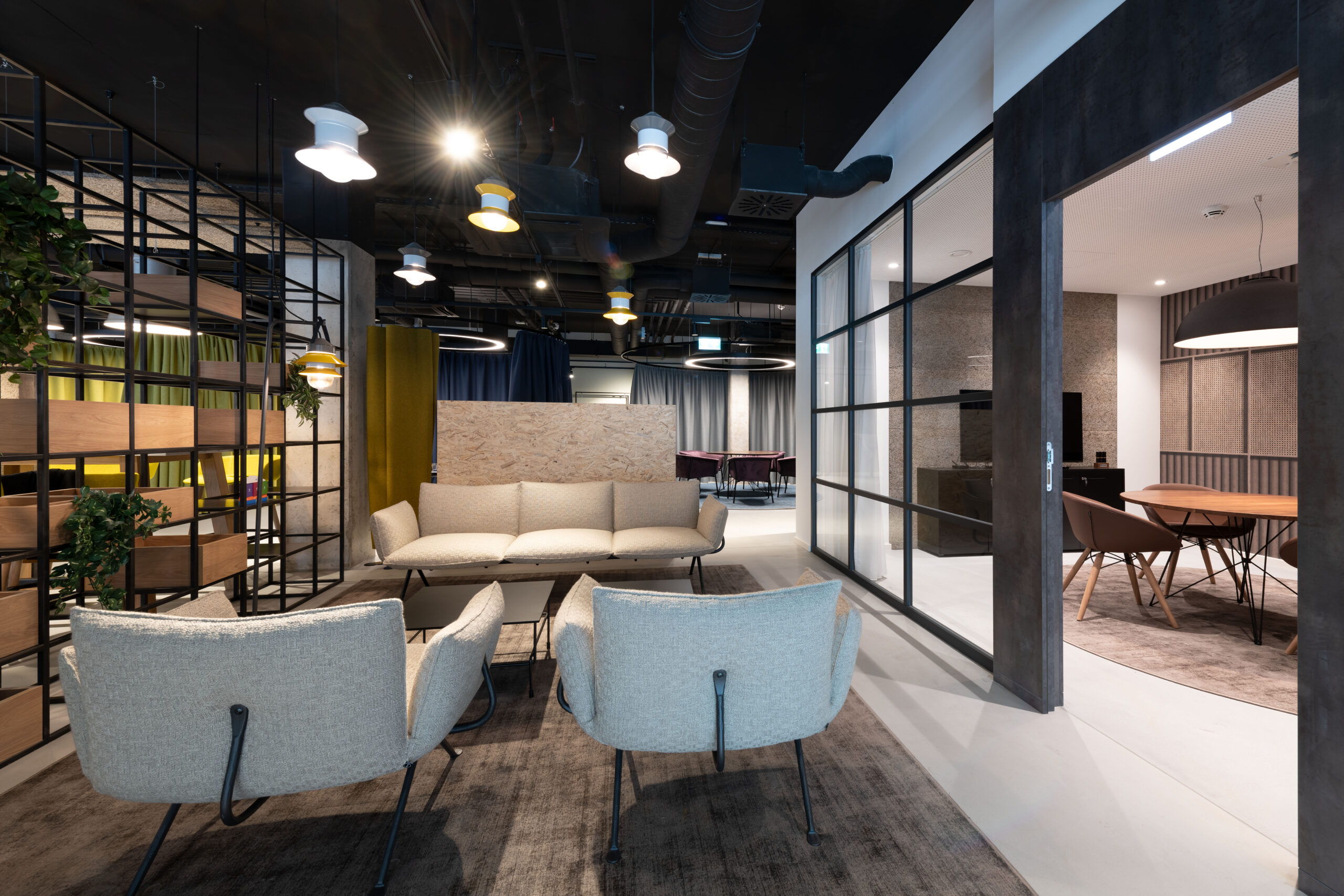 Soggiorno con divano beige, poltrone, libreria a griglia nera e porta scorrevole in vetro verso sala riunioni in legno.