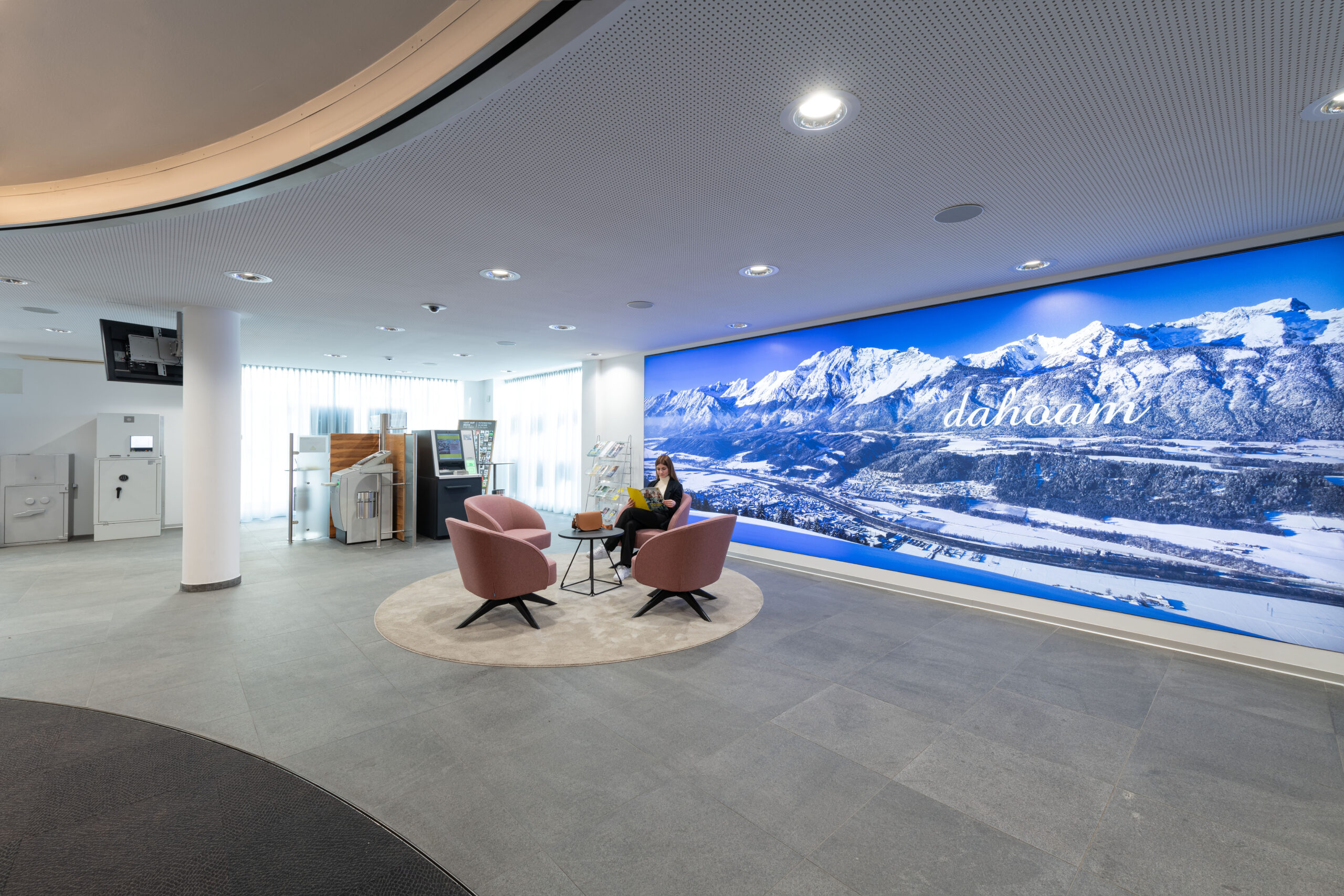 Zona attesa e area self, sedute lounge e immenso wall graphic invernale “dahoam” che raffigura le Alpi tirolesi dentro la banca Raiffeisen Regionalbank Schwaz-Wattens
