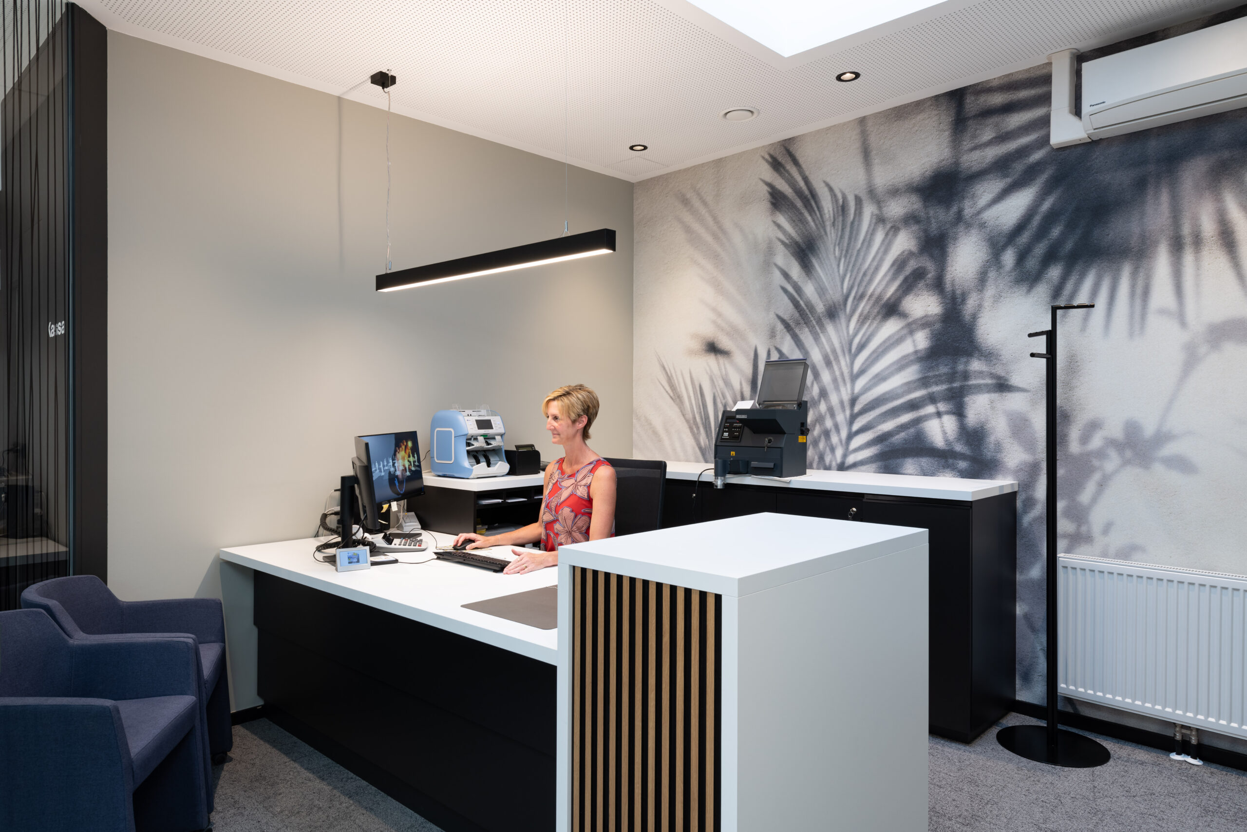 Operatrice seduta alla scrivania con stampante e decorazione murale a tema foglie su sfondo chiaro.